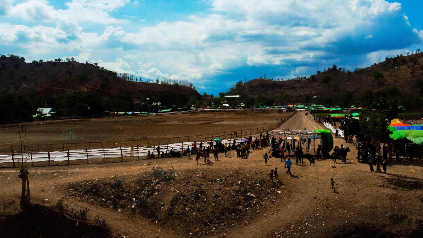 An aerial view of Bima's horse racing field, bustling with majestic horses in competition. The crowd cheers under the bright midday sun, capturing the excitement. photo
