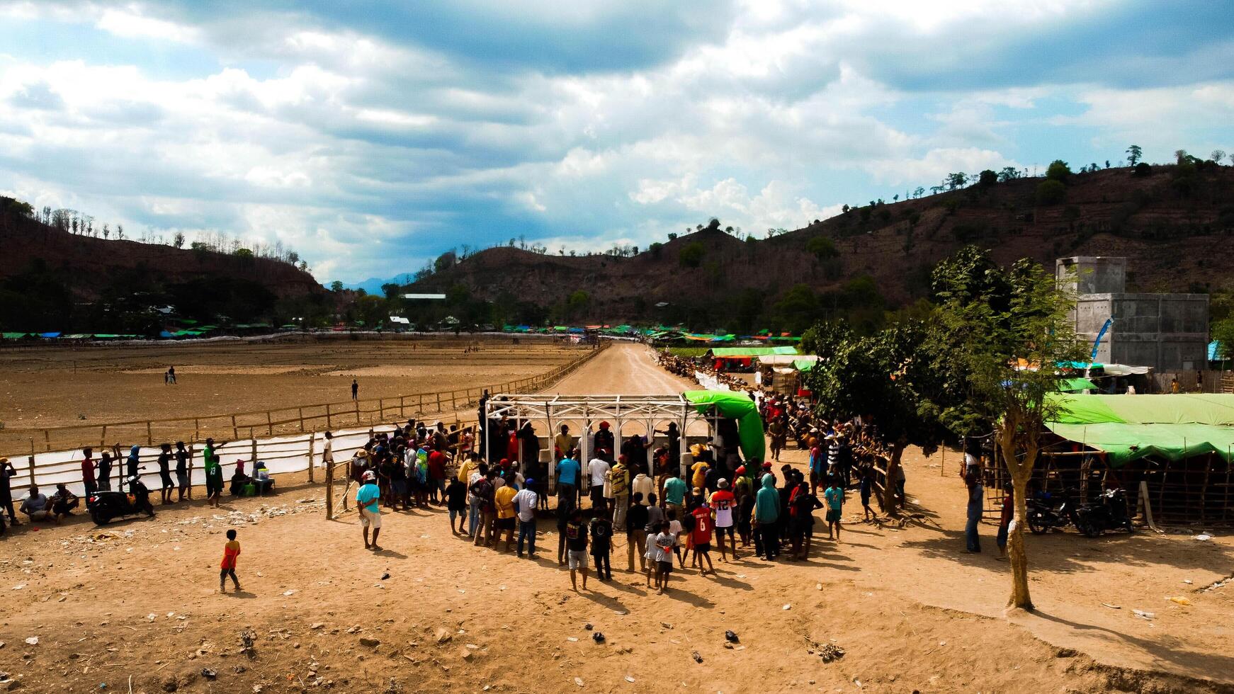 An aerial view of Bima's horse racing field, bustling with majestic horses in competition. The crowd cheers under the bright midday sun, capturing the excitement. photo
