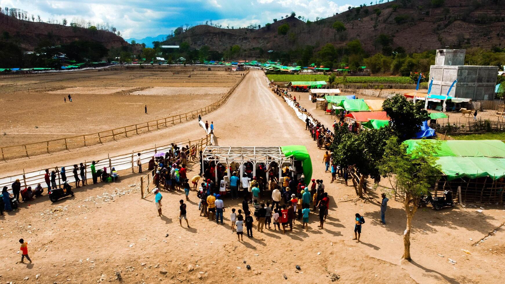 An aerial view of Bima's horse racing field, bustling with majestic horses in competition. The crowd cheers under the bright midday sun, capturing the excitement. photo