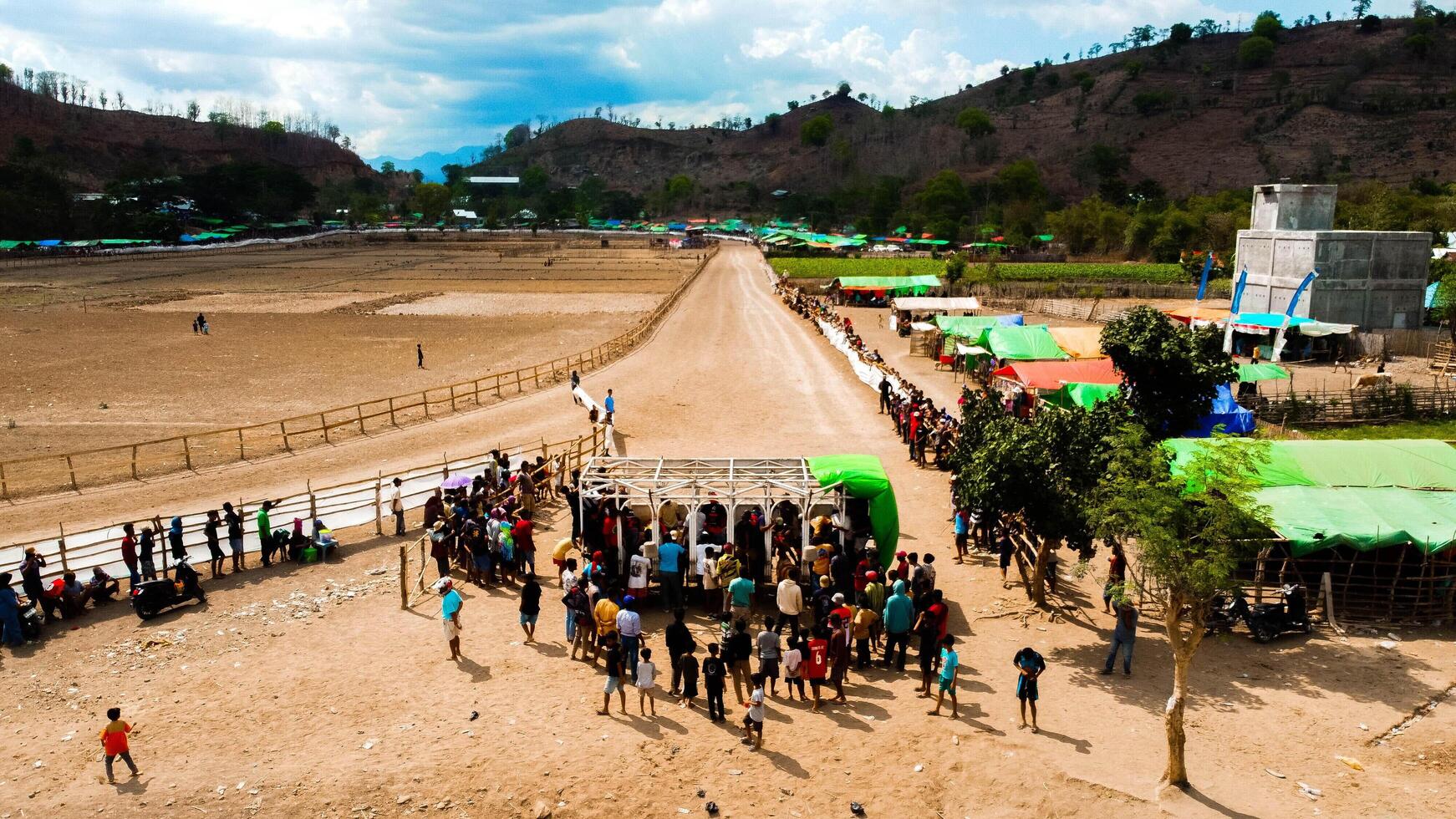 An aerial view of Bima's horse racing field, bustling with majestic horses in competition. The crowd cheers under the bright midday sun, capturing the excitement. photo
