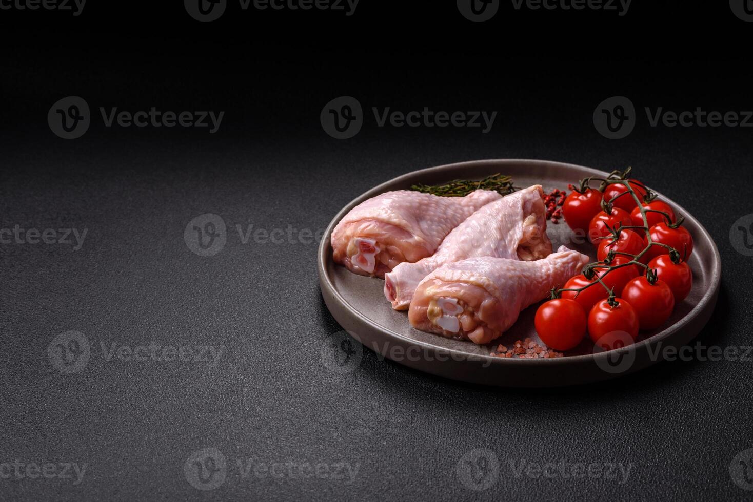 Raw chicken legs with salt, spices, herbs and tomatoes photo