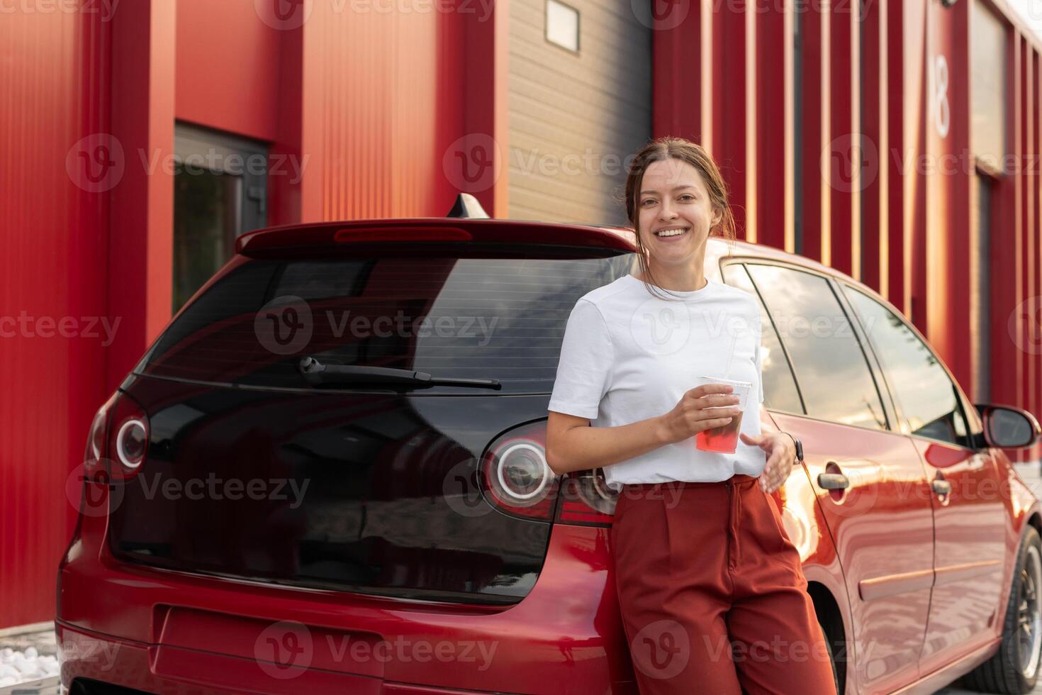 Attractive woman drinks fresh lemonade with red car on urban background photo