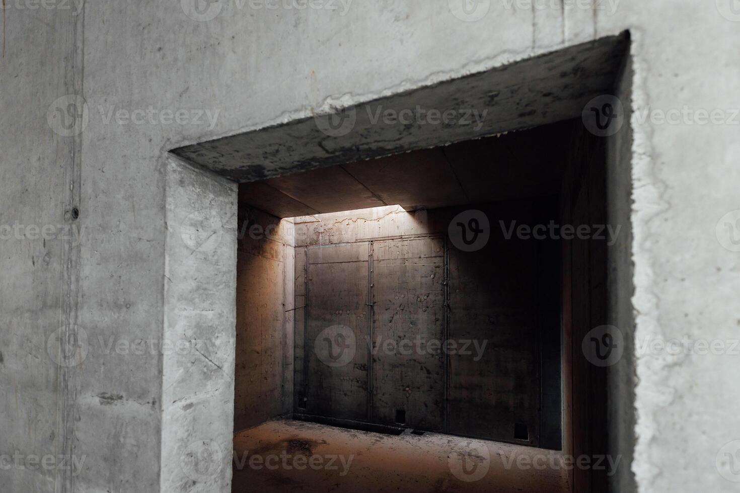 a dark room with concrete walls and a small light opening in the ceiling photo