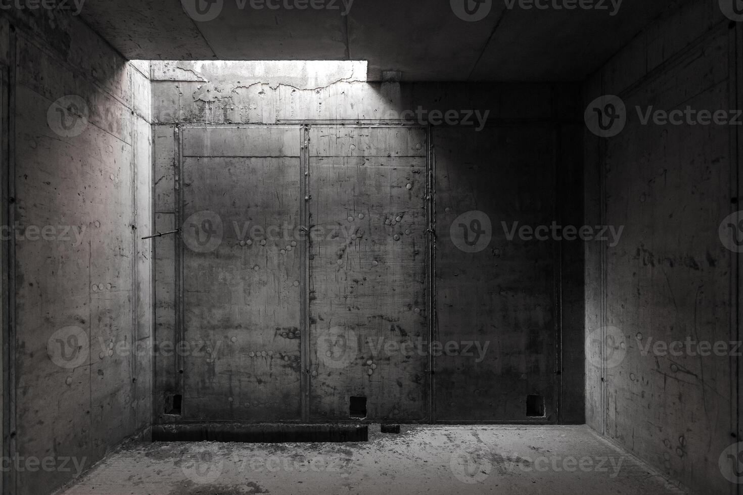 a dark room with concrete walls and a small light opening in the ceiling photo