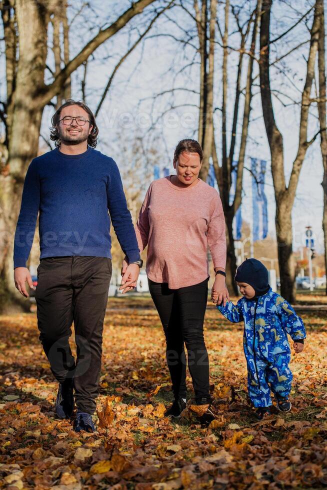 A loving couple strolls through a sunlit park with their young son, surrounded by the vibrant colors of autumn, enjoying a joyful and peaceful family moment together. photo