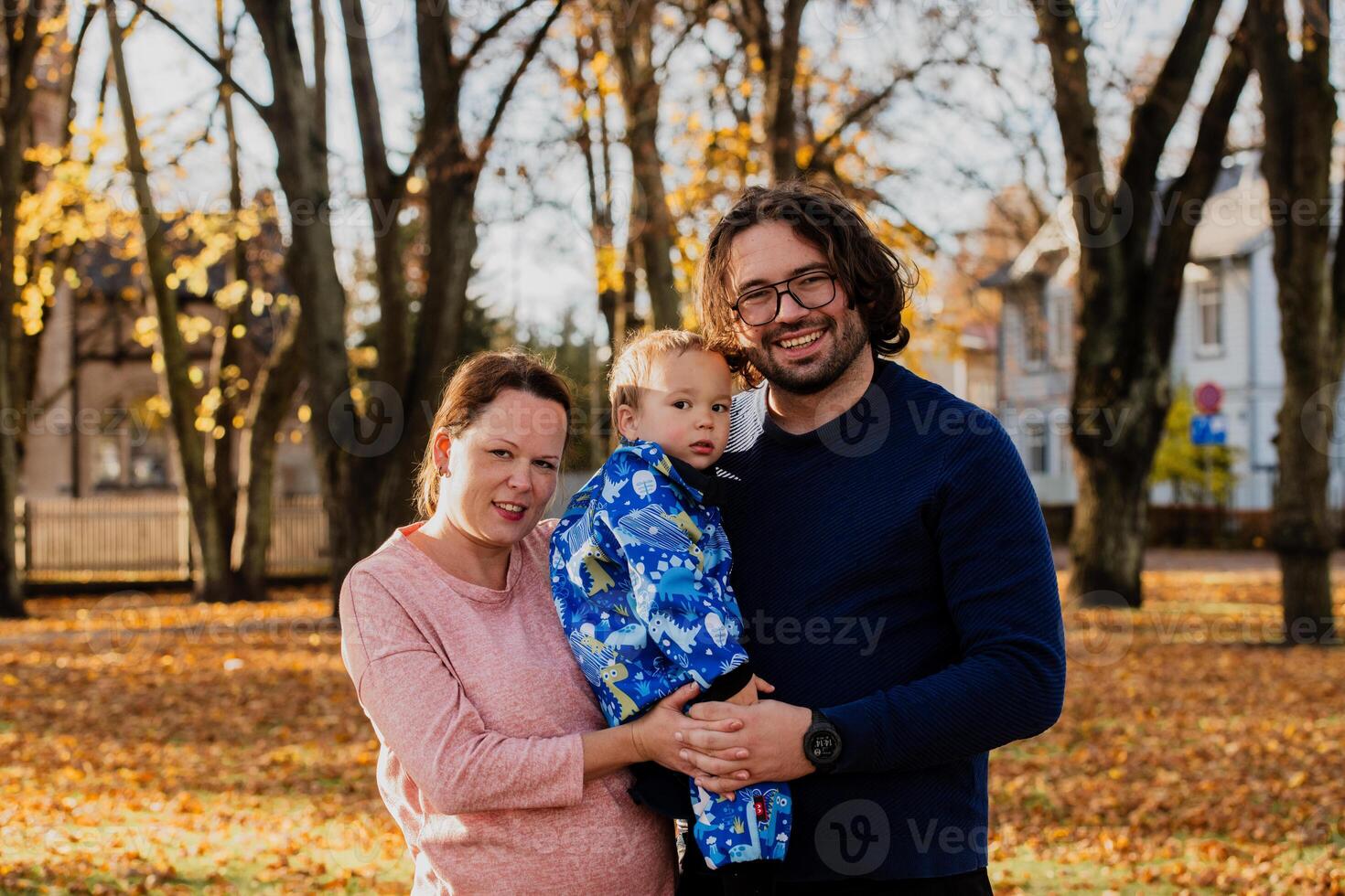 On a sunny autumn day in the park, a mother and father lovingly embrace their young son, sharing moments of laughter and joy as they play together photo