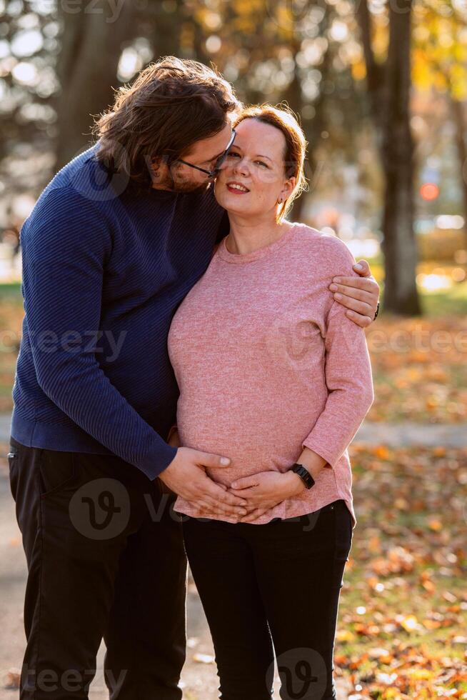 A man lovingly embraces his pregnant wife in the park, sharing a peaceful moment of warmth and affection photo