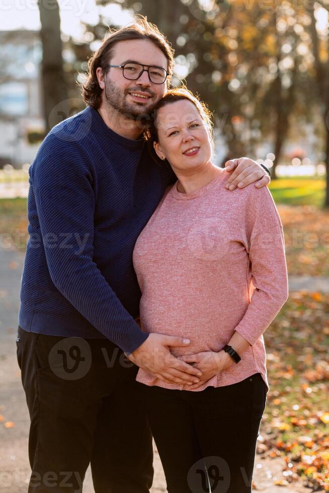 A man lovingly embraces his pregnant wife in the park, sharing a peaceful moment of warmth and affection photo
