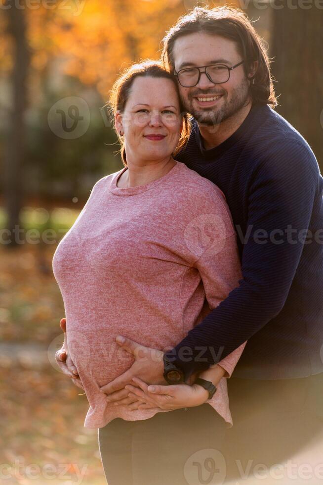 A man lovingly embraces his pregnant wife in the park, sharing a peaceful moment of warmth and affection photo