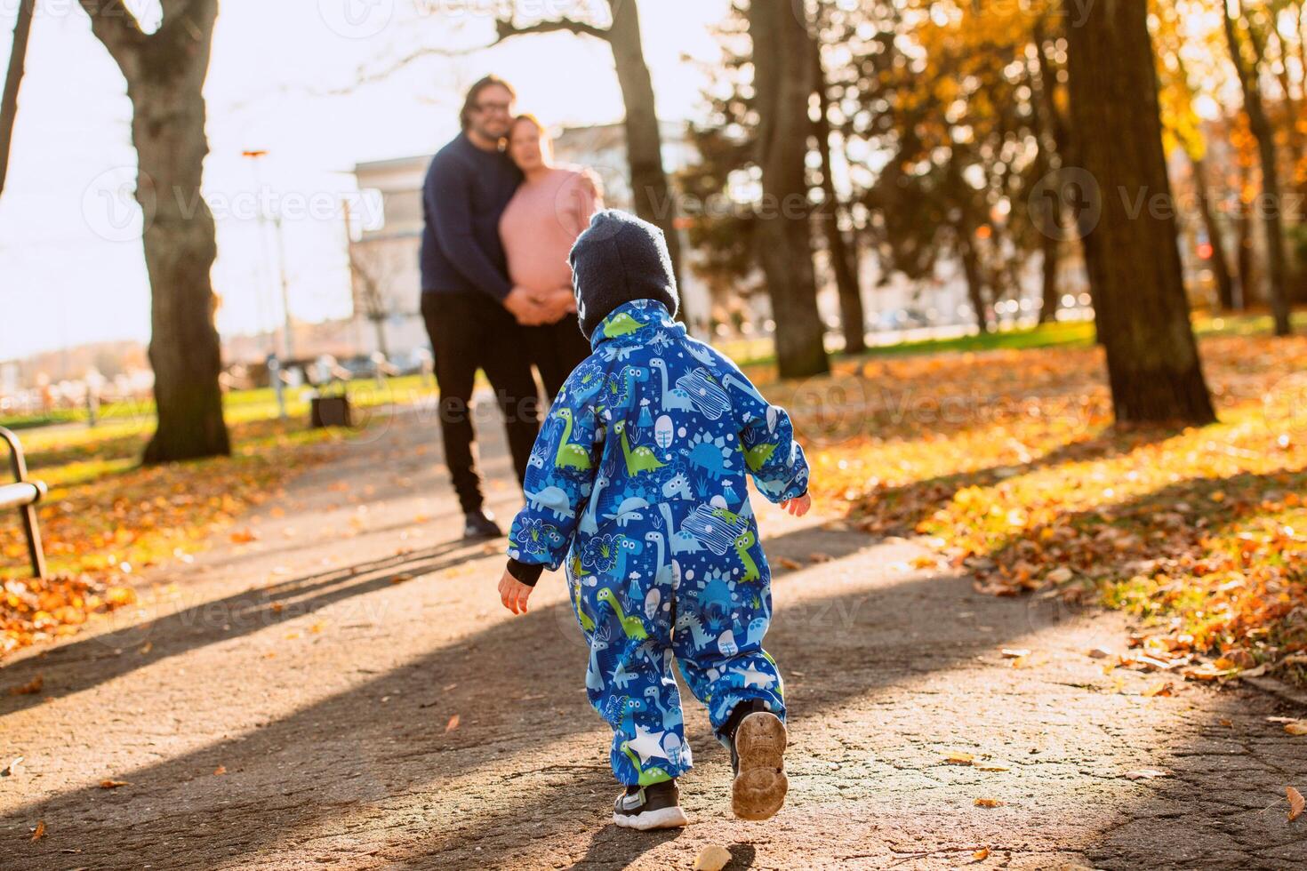 A joyful little boy in his winter coat and hat plays happily in the park, surrounded by the love and warmth of his smiling parents photo