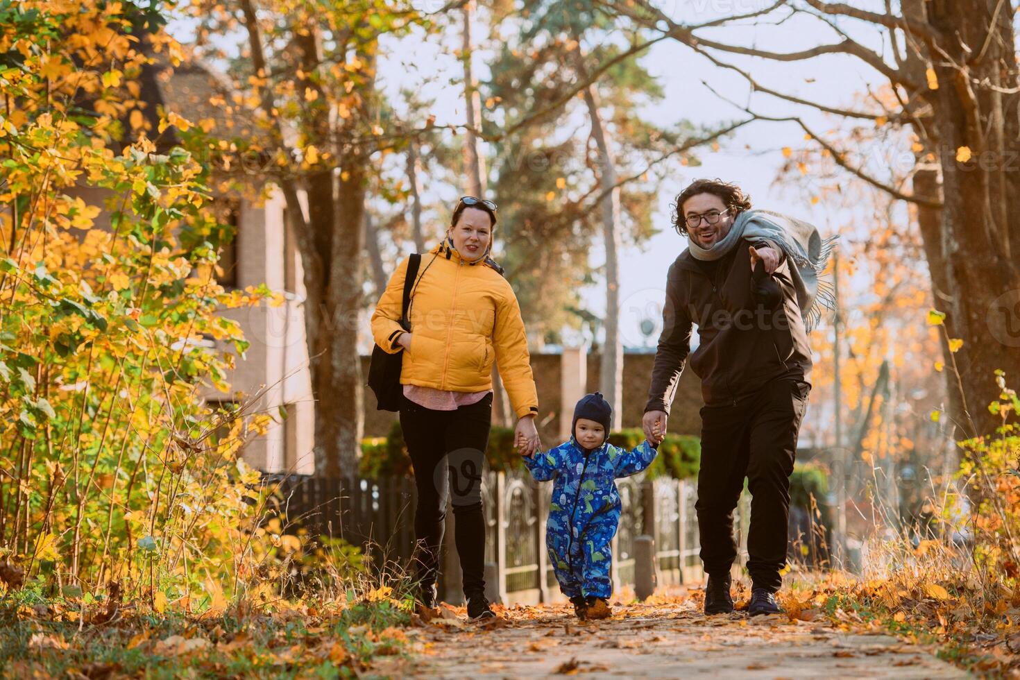 A loving couple strolls through a sunlit park with their young son, surrounded by the vibrant colors of autumn, enjoying a joyful and peaceful family moment together. photo