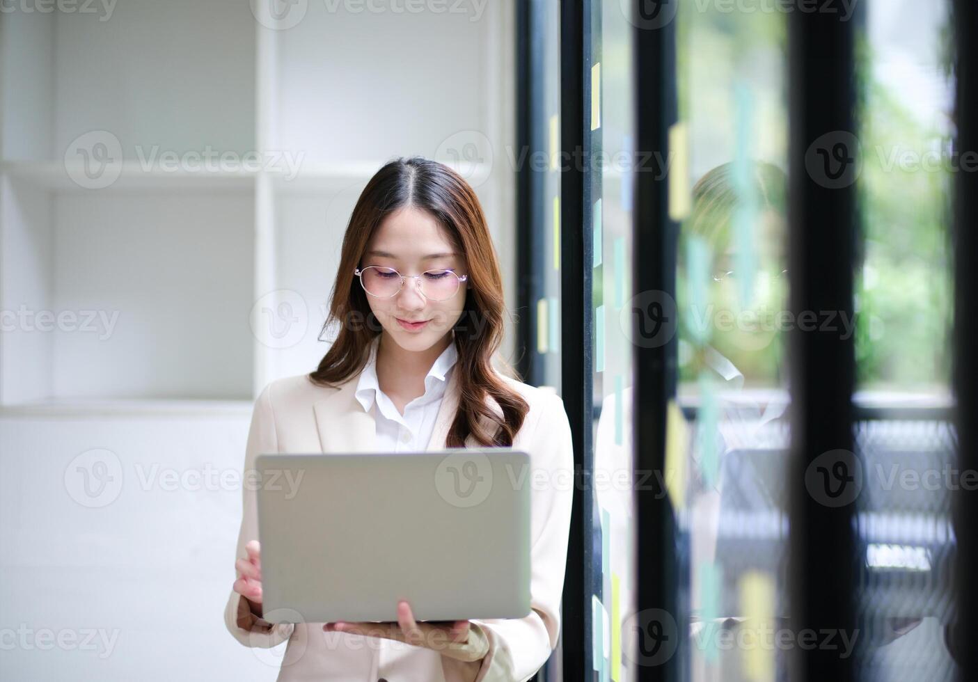 Businesswoman using a laptop and reviewing data with sticky notes in the background. photo