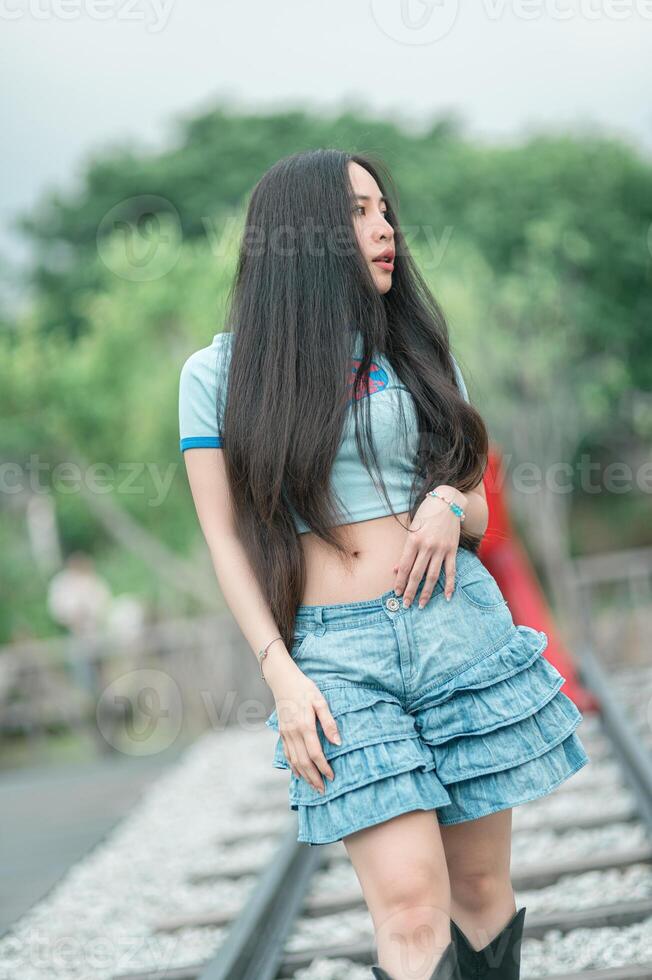 A woman in a blue shirt and denim shorts standing on a railroad track photo