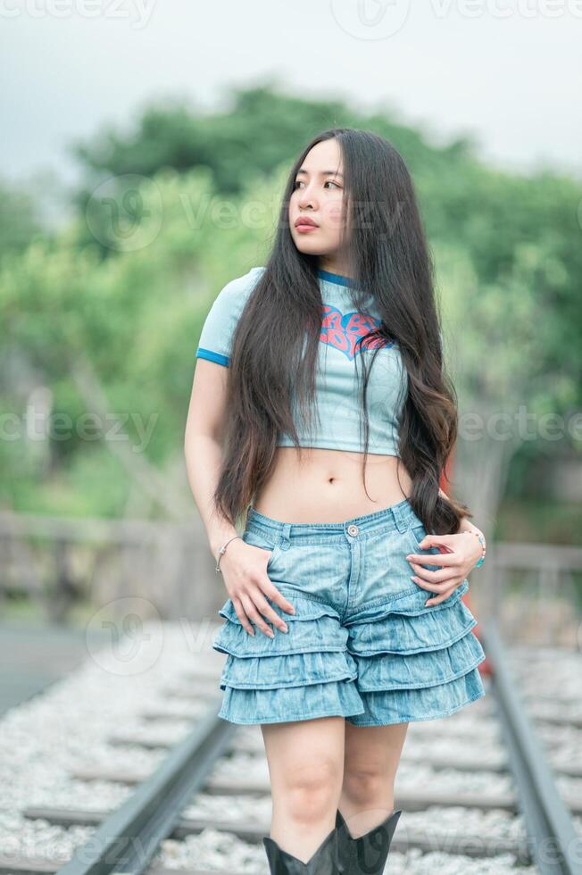 A woman in a blue shirt and denim shorts standing on railroad tracks photo