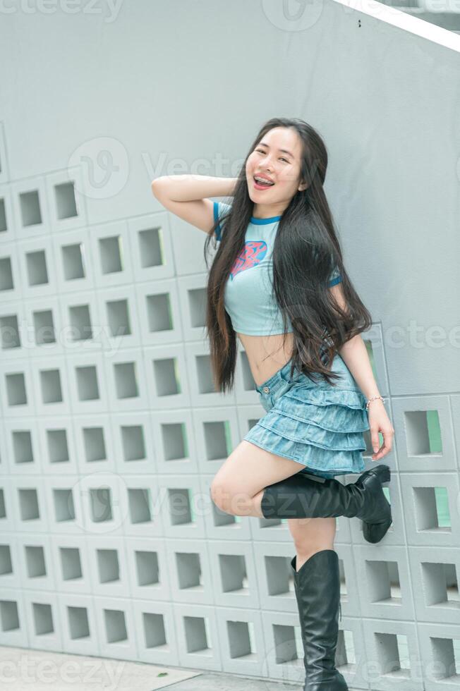 A woman in a short skirt and boots leaning against a wall photo
