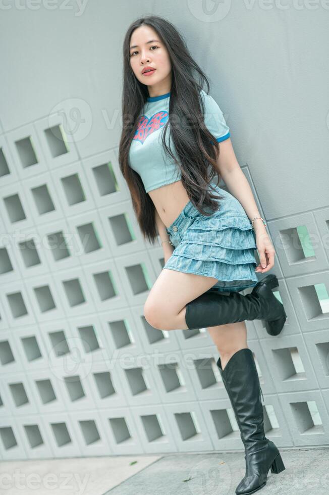 A woman in a blue shirt and skirt posing against a wall photo