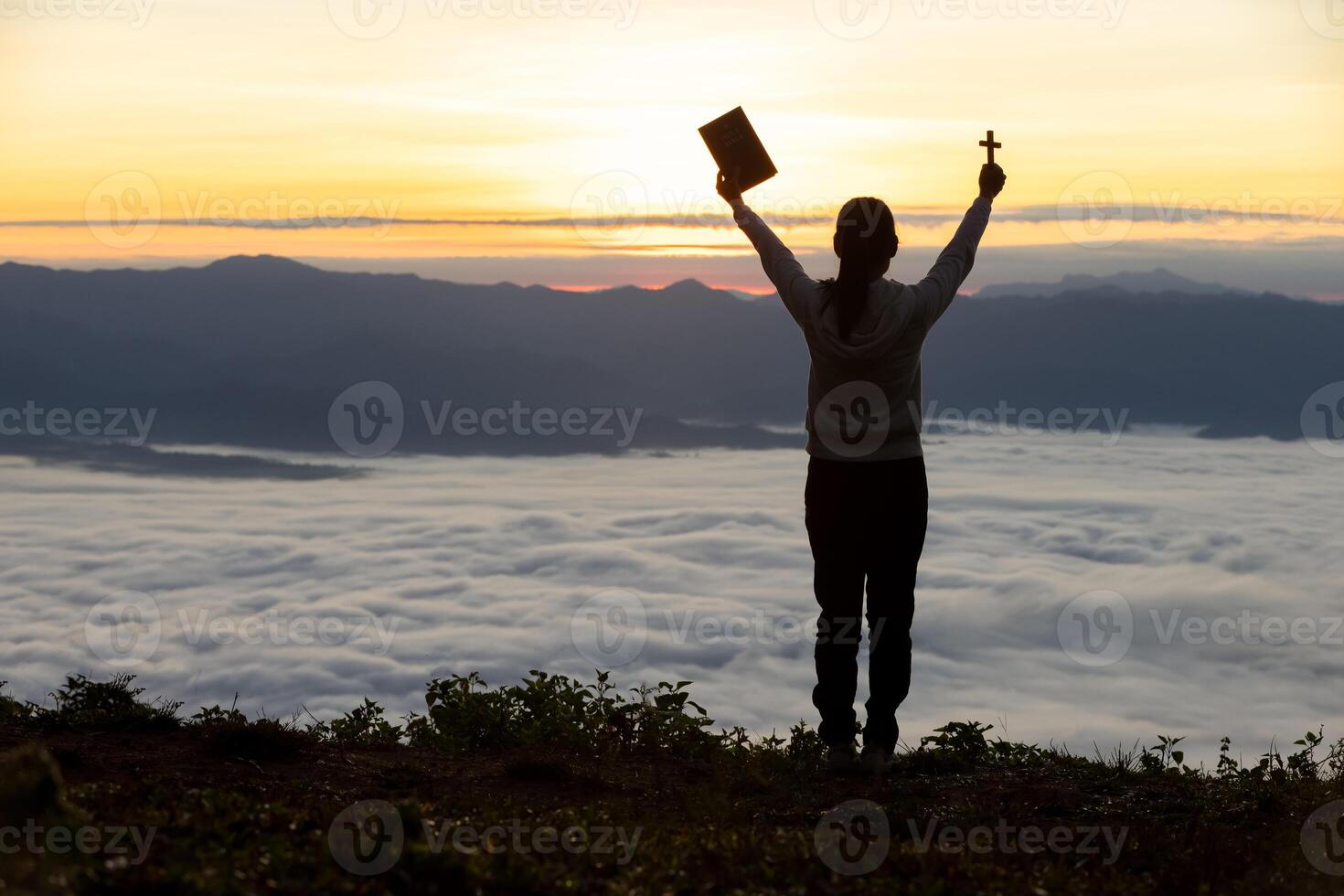 Silhouette of a woman praying on a mountain at sunrise. Young woman praying to God. photo