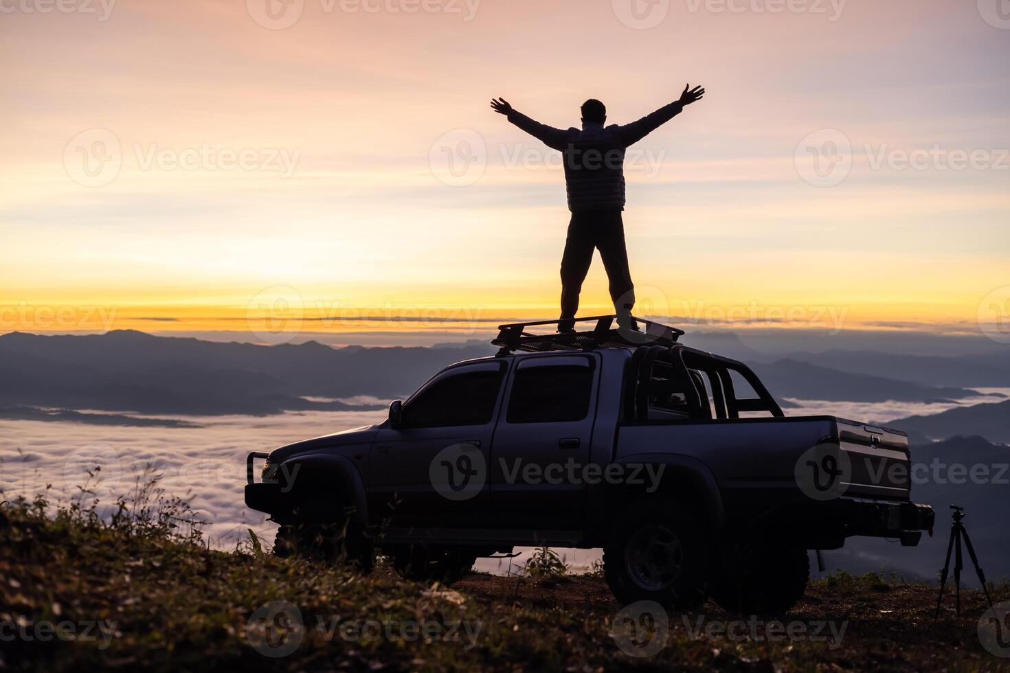 Silhouette of a man praying on the roof of a car on a mountain at sunrise. photo
