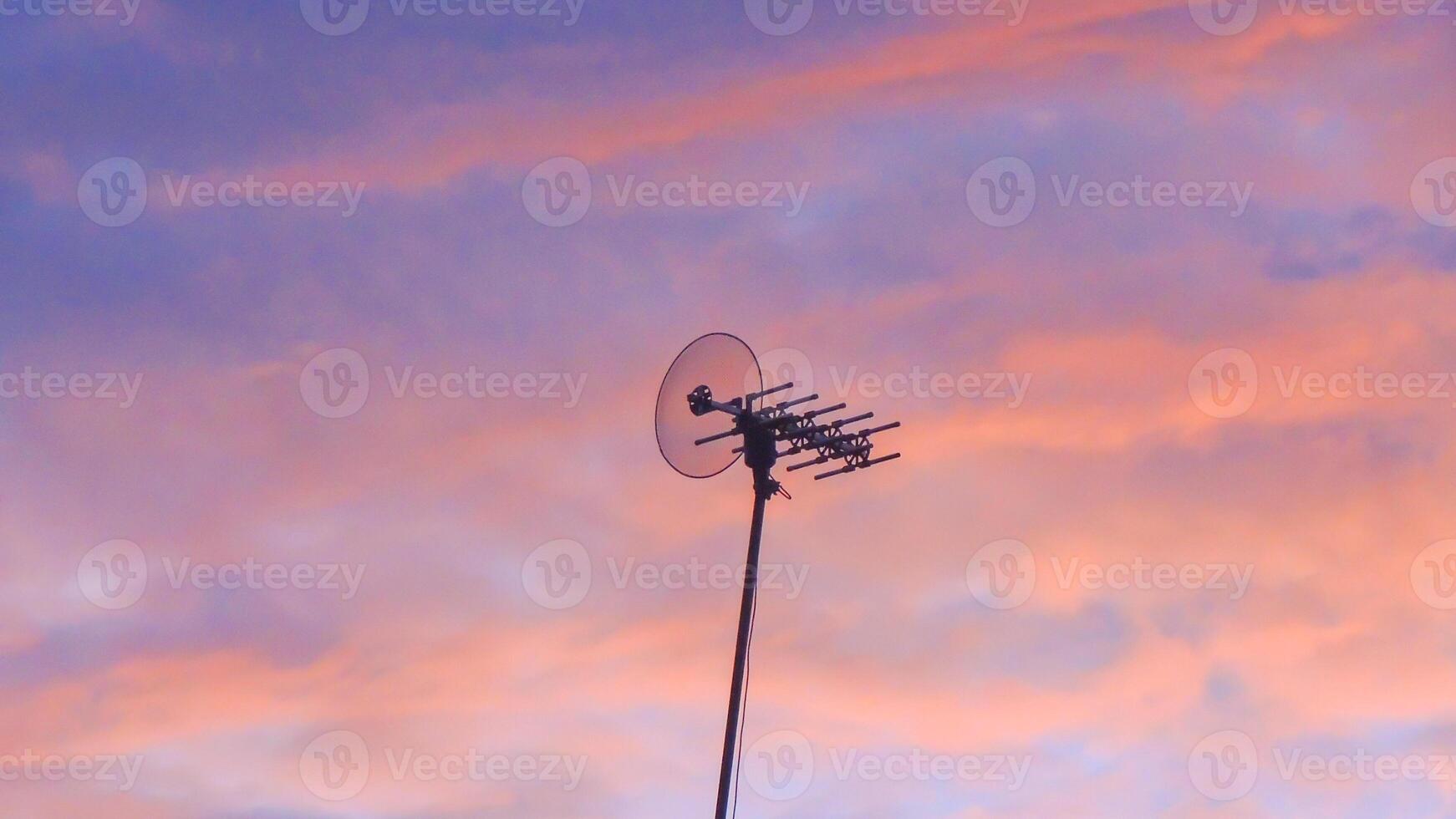 A television antenna is shown in silhouette against a pink sky photo