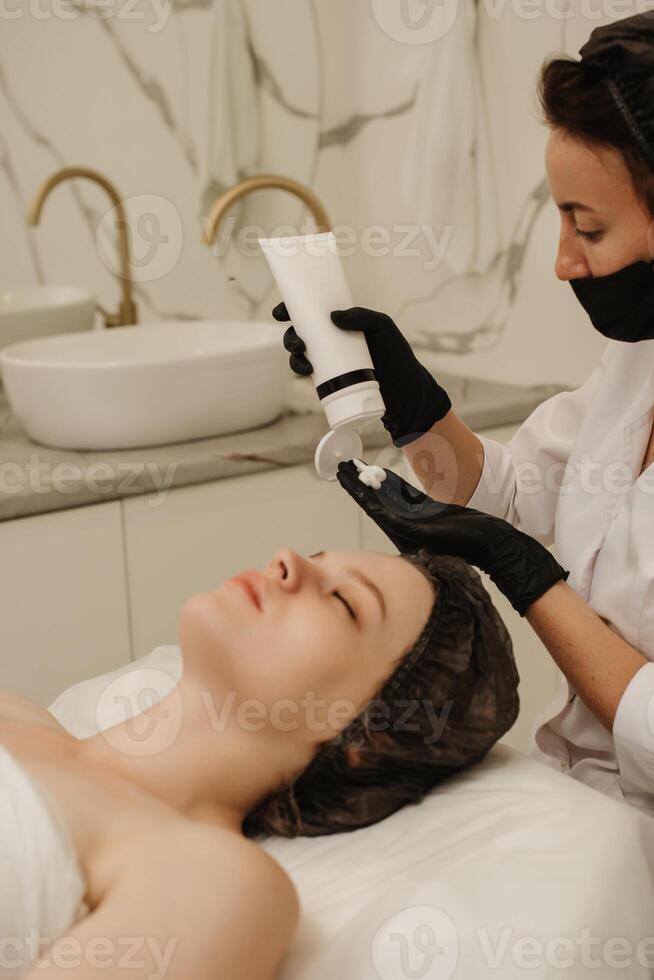 Close-up of the beautician's hands applying cream to the client's face and doing a massage. Facial skin care. Vertical photo
