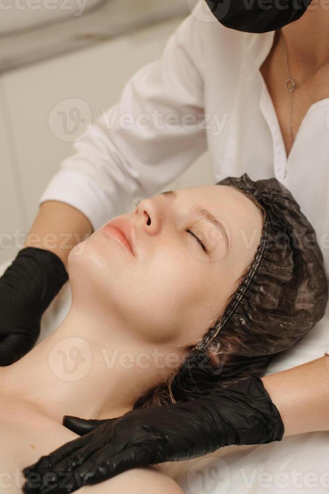 Top view of a qualified massotherapist woman's hands massaging female client facial skin. Beauty treatment concept. vertical photo. photo