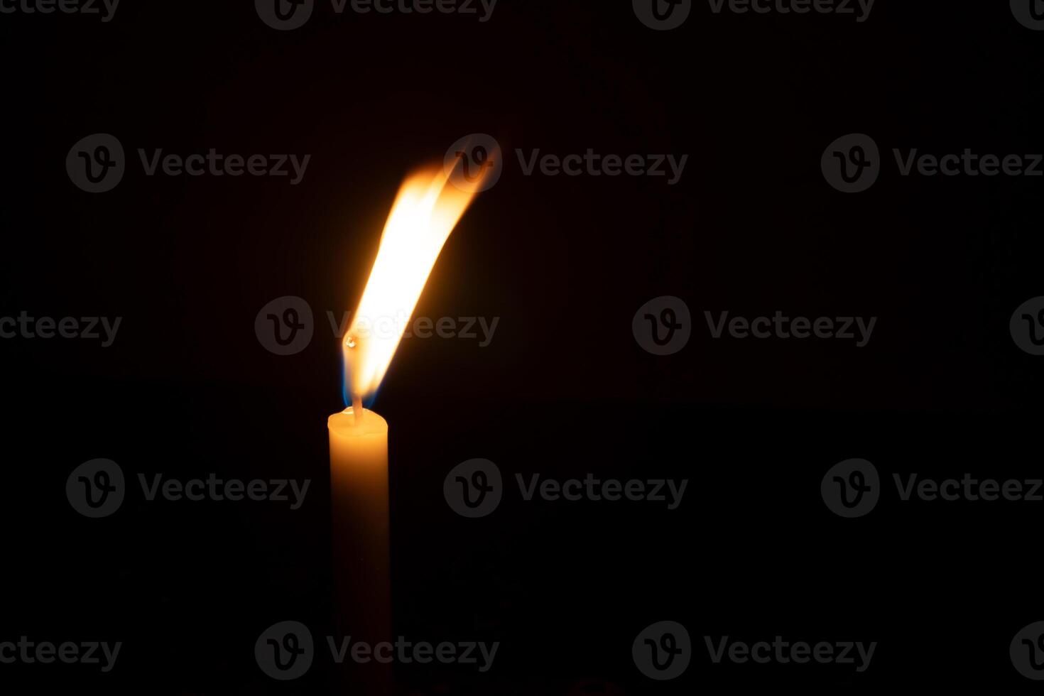 A single burning candle flame or light glowing on a small orange candle on black or dark background on table in church for Christmas, funeral or memorial service with copy space photo