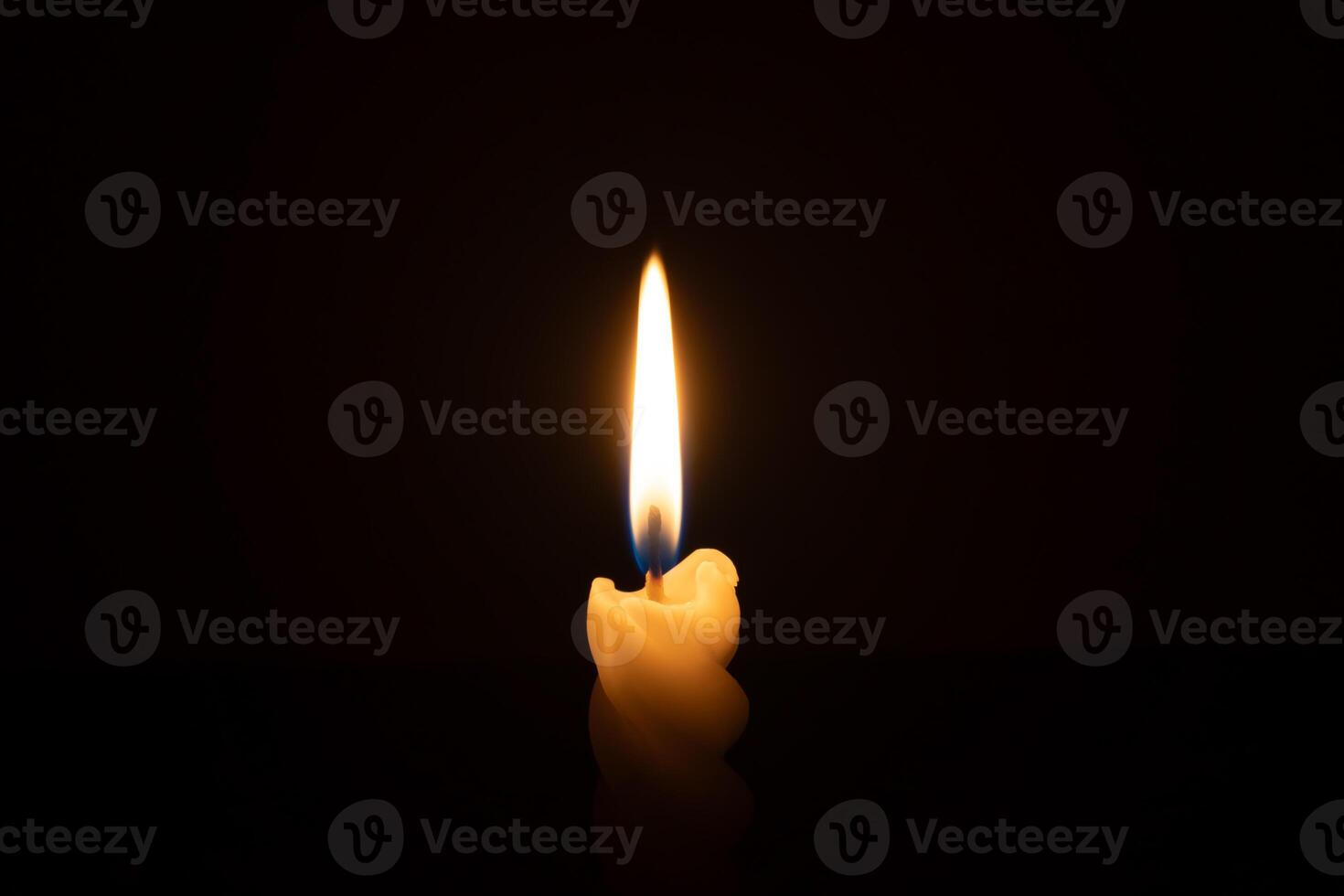 A single burning candle flame or light glowing on a spiral white candle on black or dark background on table in church for Christmas, funeral or memorial service with copy space photo