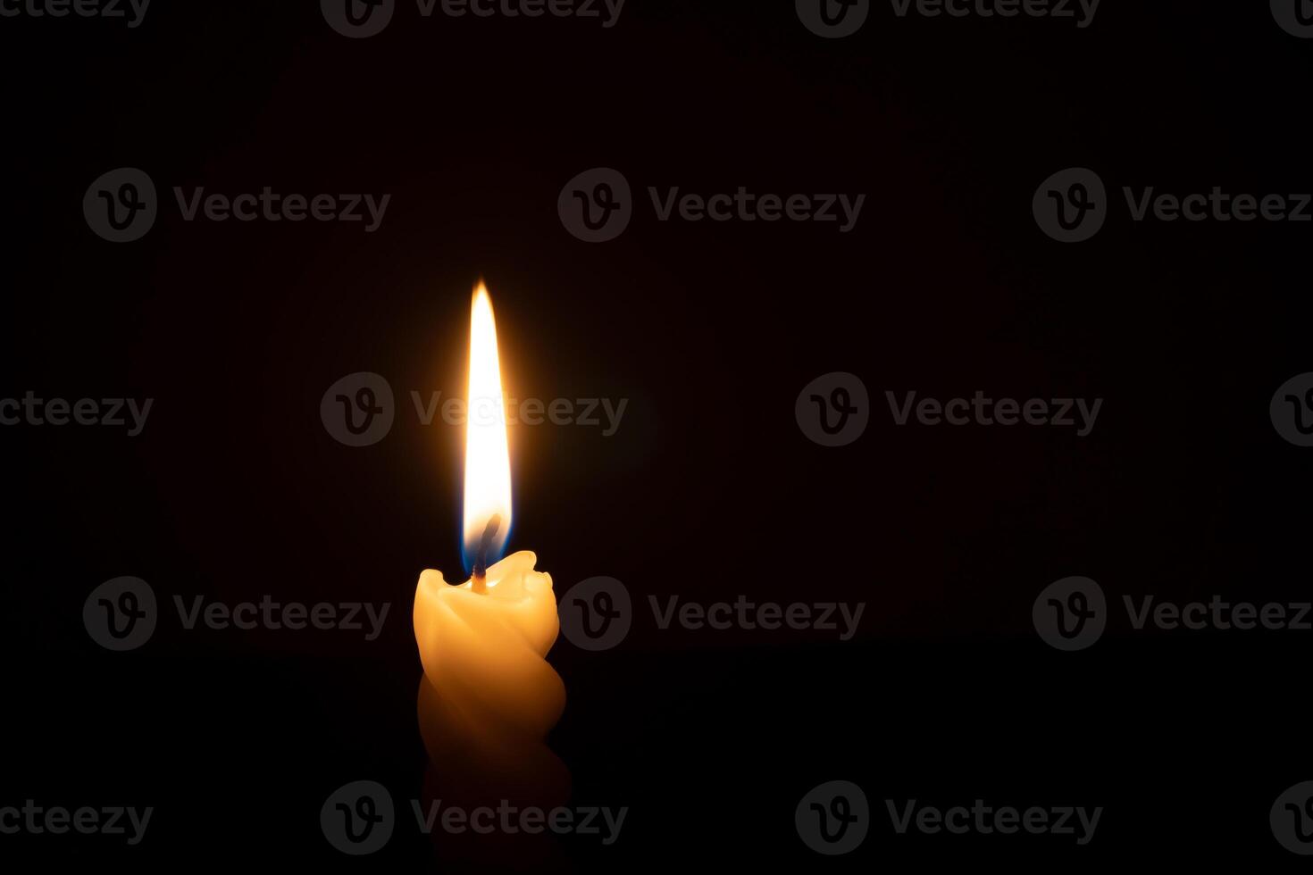 A single burning candle flame or light glowing on a spiral white candle on black or dark background on table in church for Christmas, funeral or memorial service with copy space photo