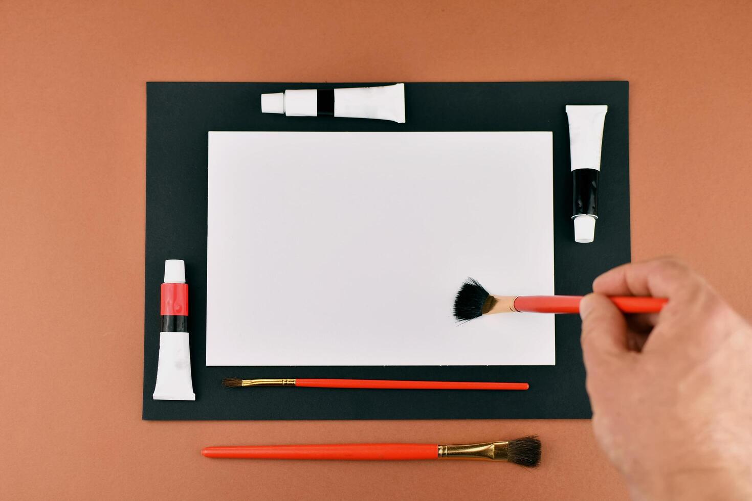 A person holding a brush and a piece of paper next to a box of paint photo
