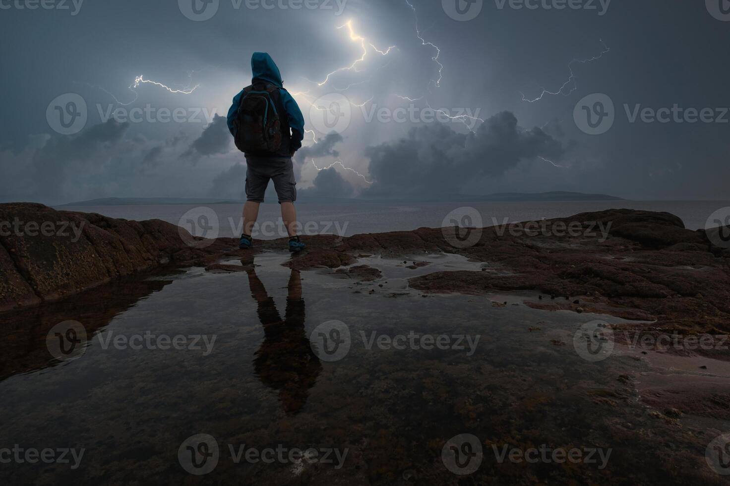 A person standing on a rock with a backpack photo