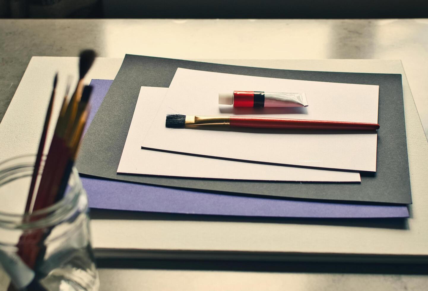 A table with a paintbrush, paper, and a jar photo