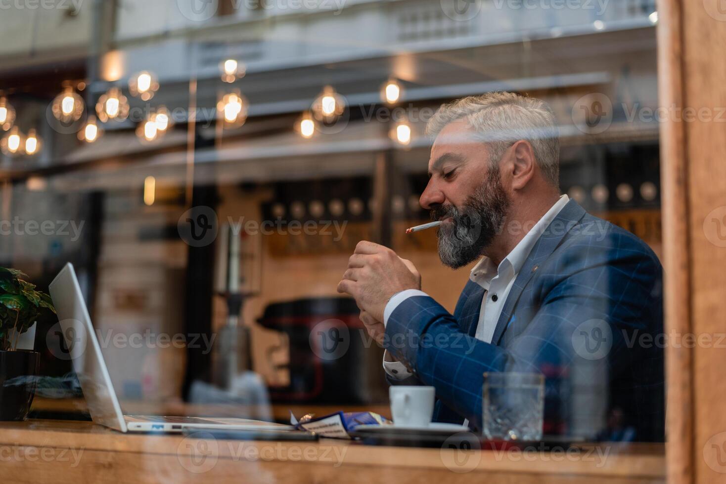 A handsome mature business man using his laptop at a restaurant cafe drinking coffee and smoking a cigarette. photo