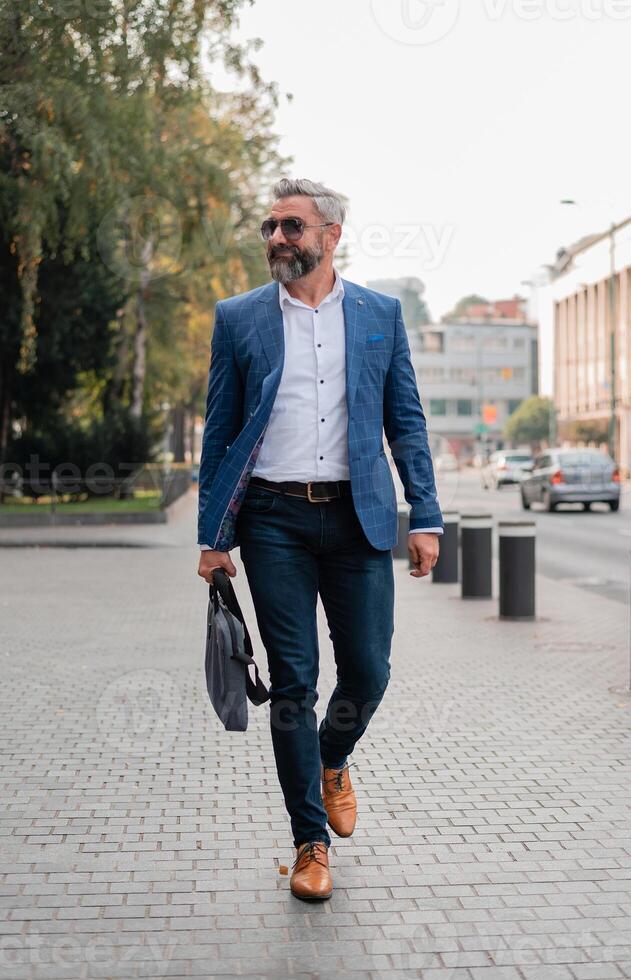 A handsome mature business man is walking through the city street. photo
