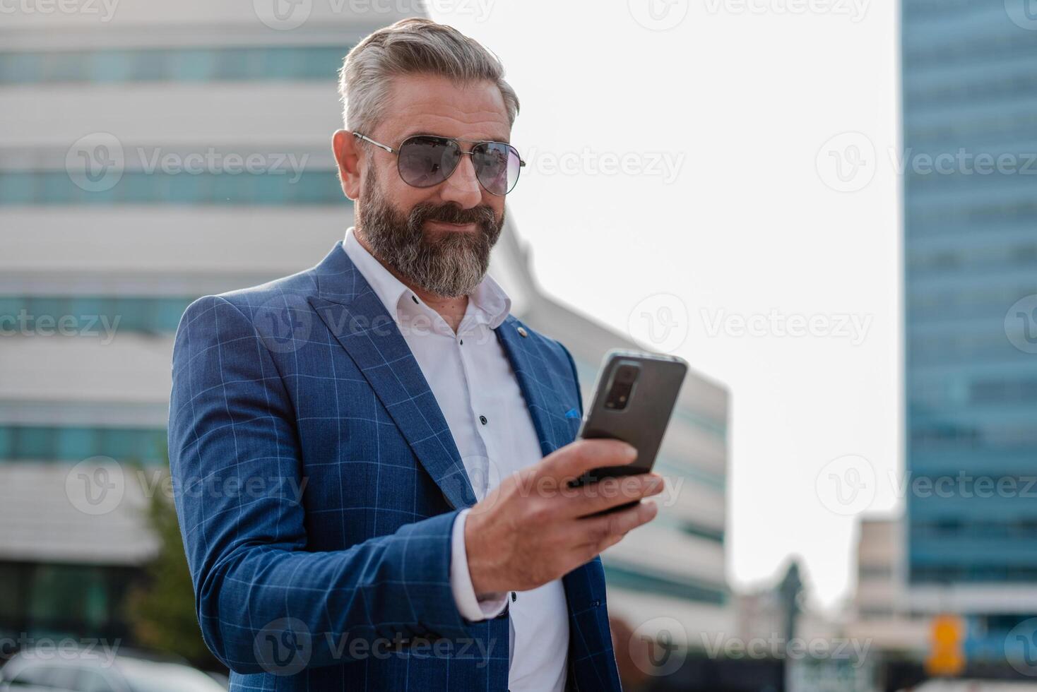 A happy mature business man using a mobile phone app texting outside of the office in the city with urban buildings in the background. photo