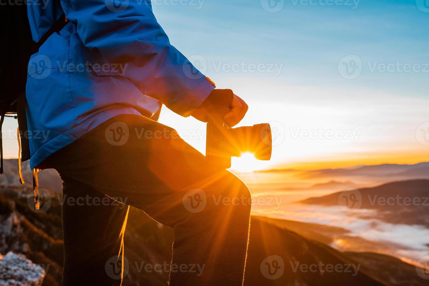 A male photographer taking a photo on the mountain top at sunrise or sunset adventure travel photography.