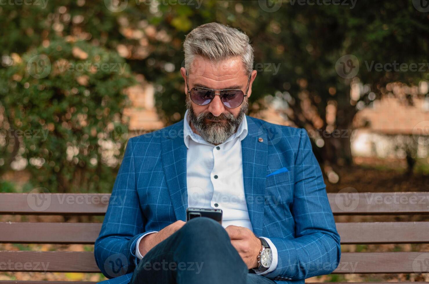 A hipster mature business man using mobile phone app texting while sitting on the park bench. photo