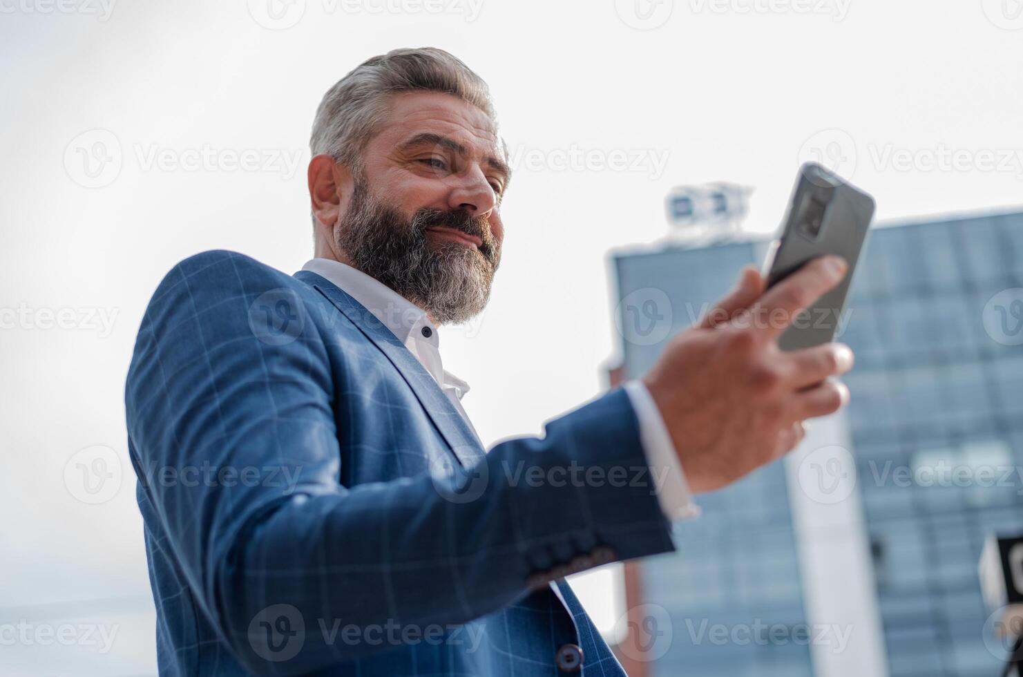A happy mature business man using mobile phone app texting outside of office in city with urban buildings in the background. photo