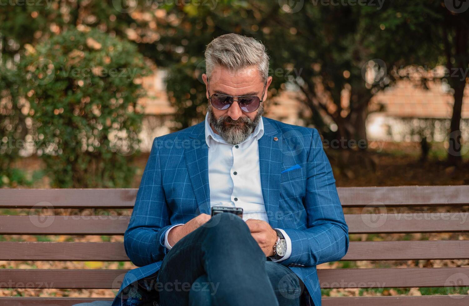 A hipster mature business man using mobile phone app texting while sitting on the park bench. photo