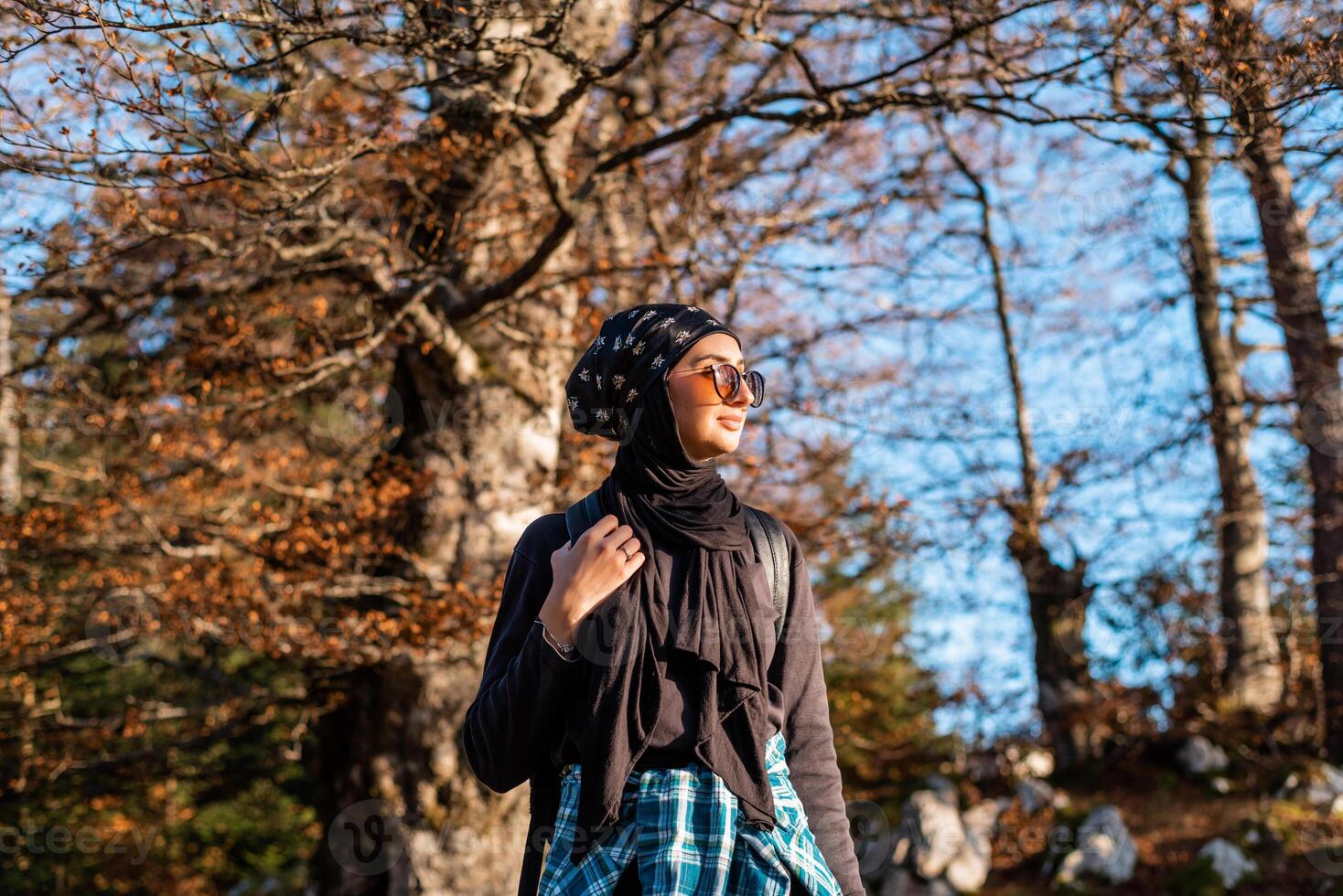 A happy woman in hijab enjoying in nature while walking in the autumn forest. photo