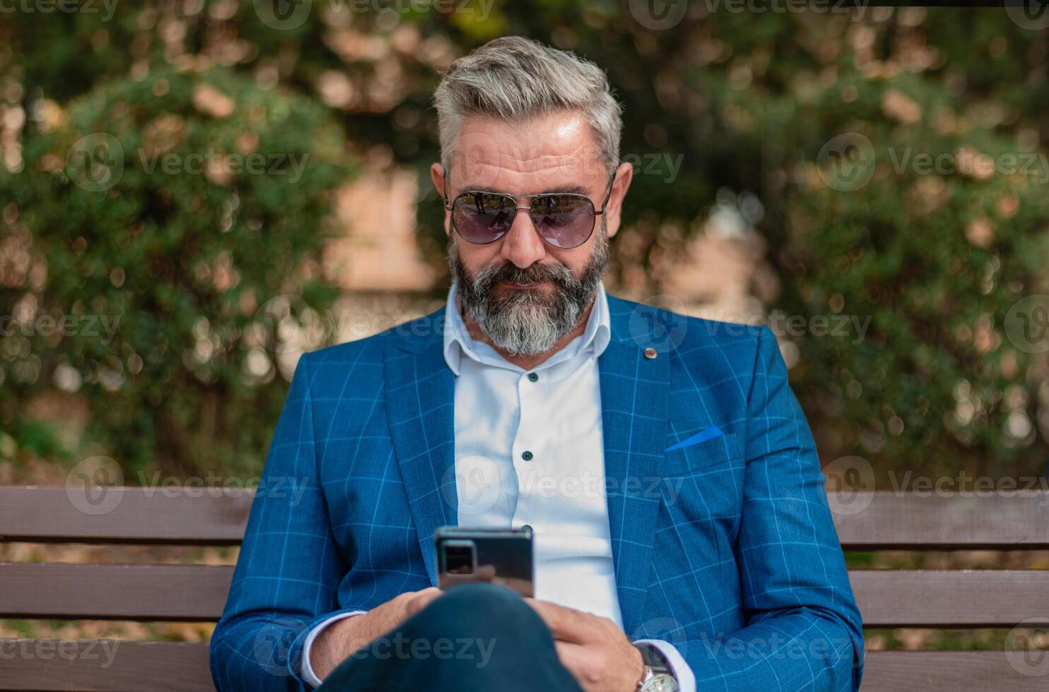 A hipster mature business man using mobile phone app texting while sitting on the park bench. photo