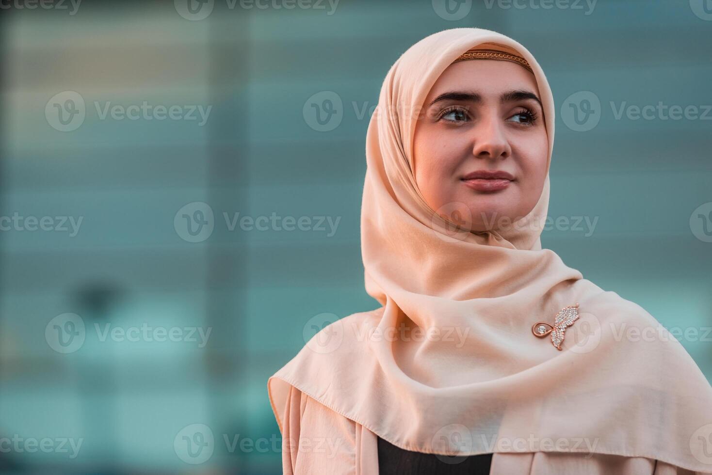 Portrait of a young happy Muslim business woman in hijab with a modern office building on the background. photo