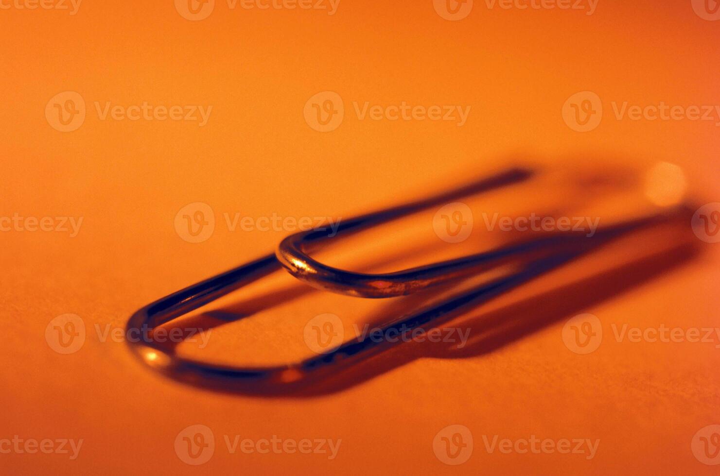 Close-Up of a Single Paperclip on Orange Background photo