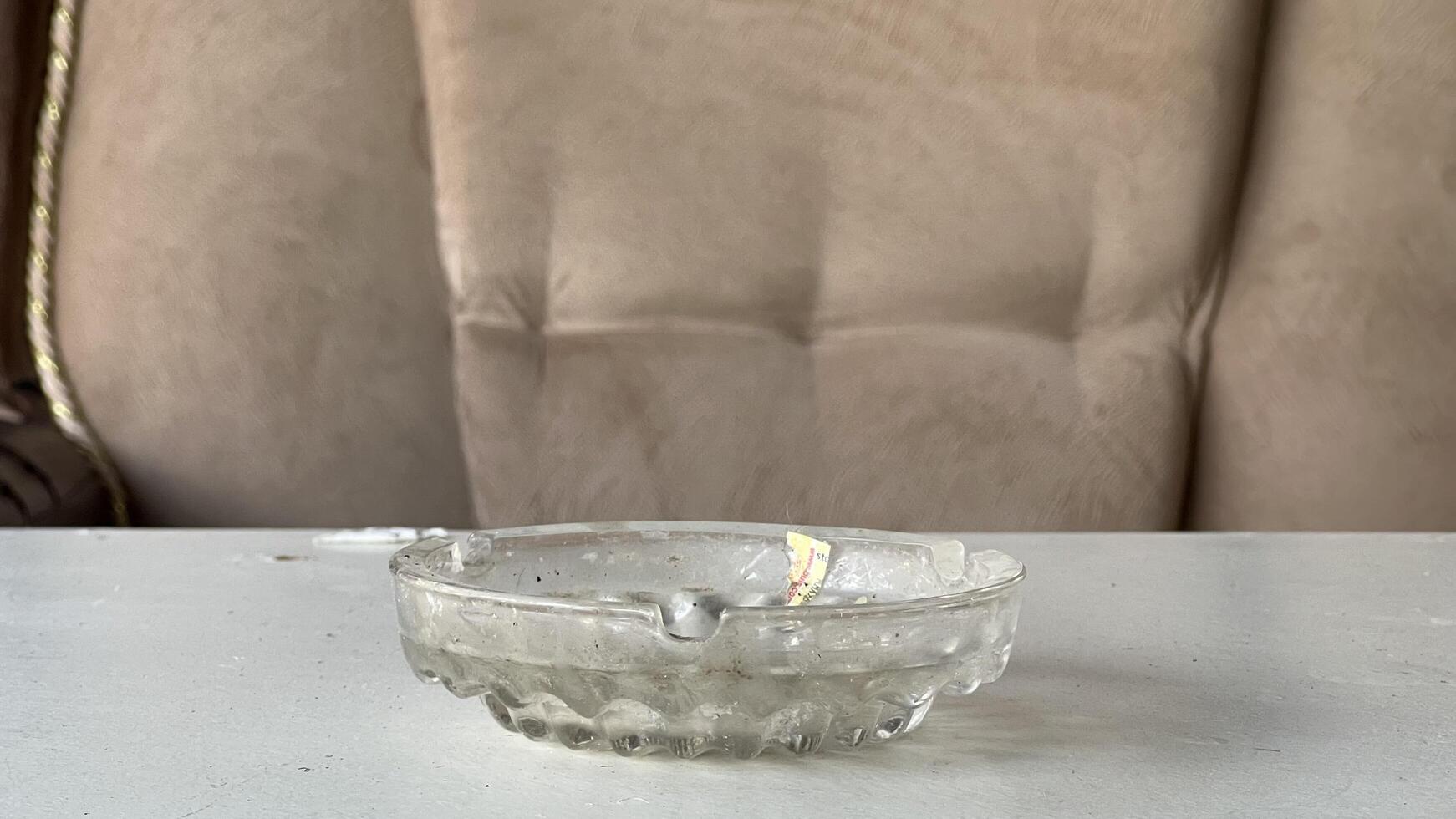 Clear glass ashtray placed on a table beside a soft couch photo