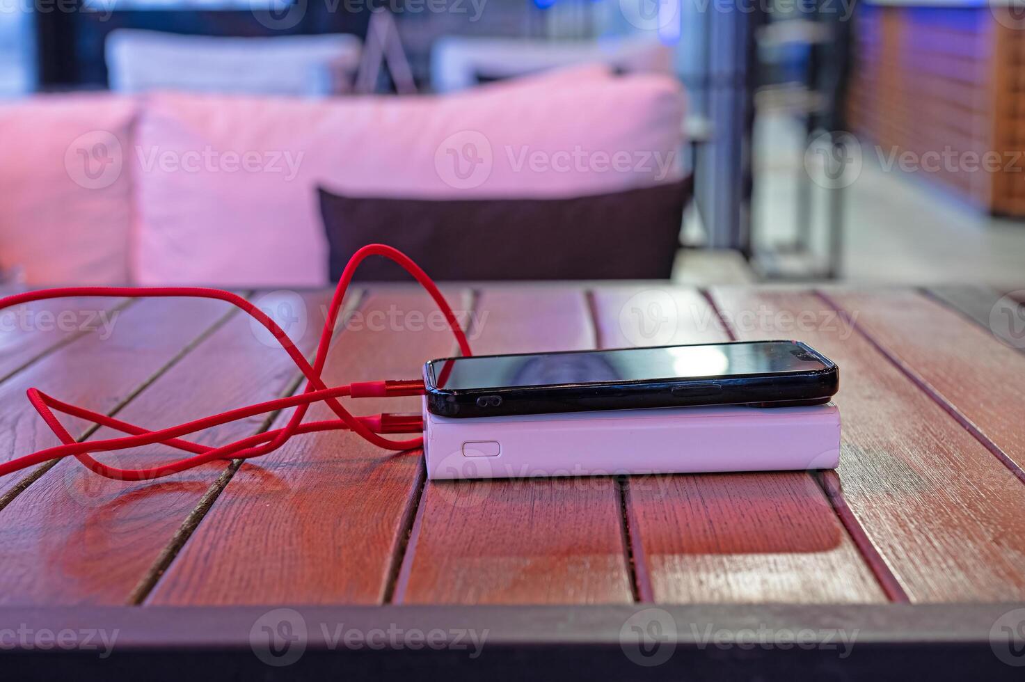 Black smartphone charged with a power bank on a wooden floor. photo