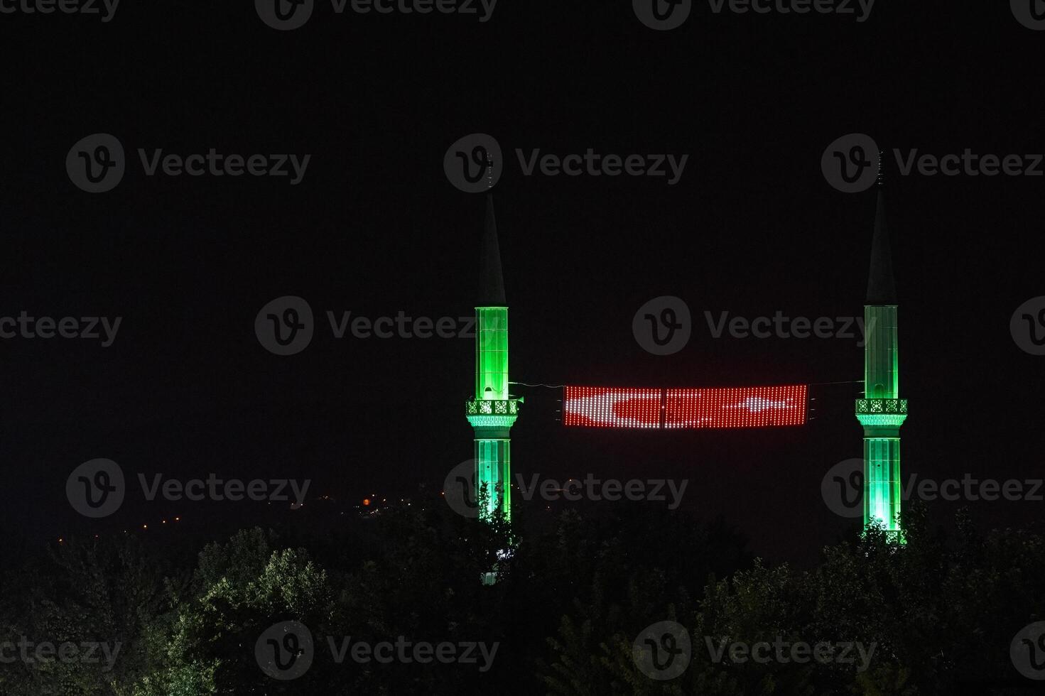 Two minarets with green lights at night and a Turkish flag between them. photo