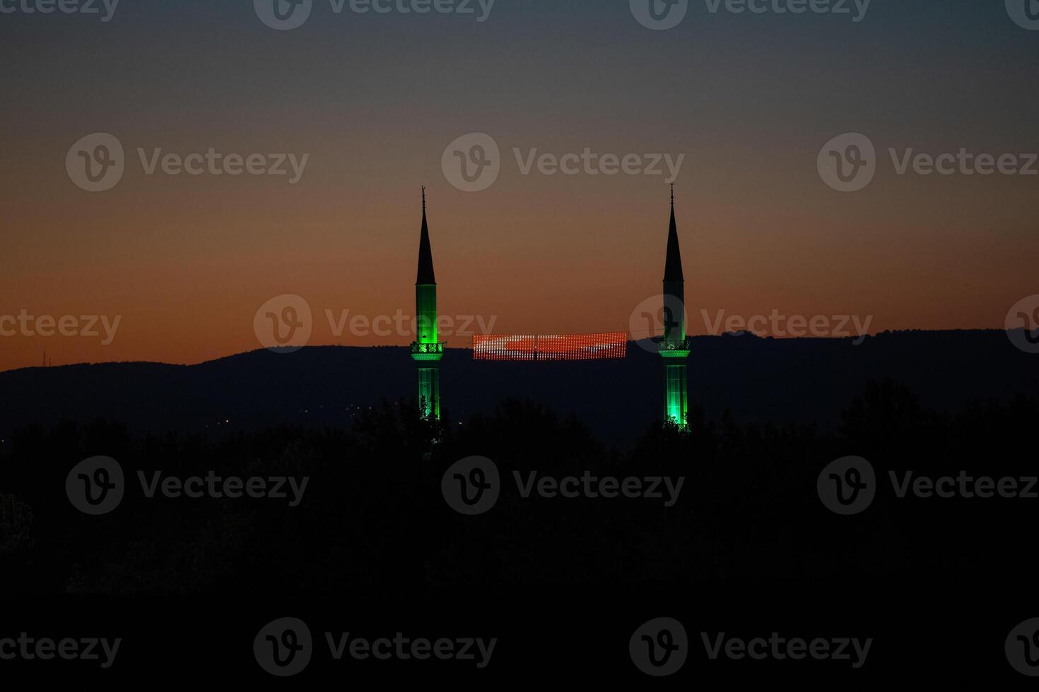 Two minarets with green lights at night and a Turkish flag between them. photo