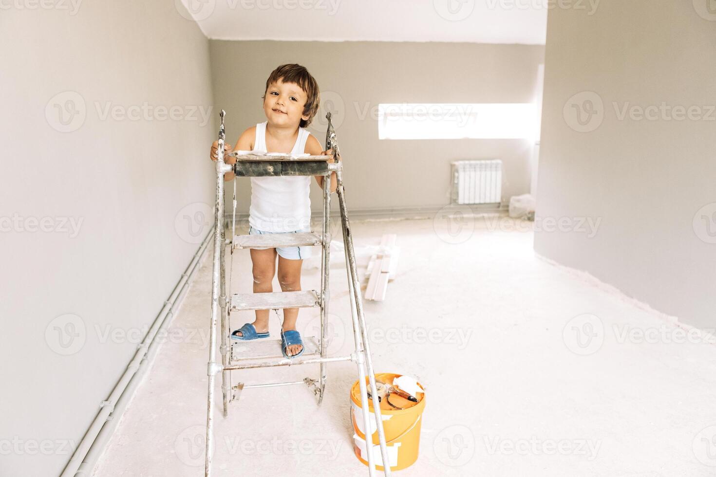 A little boy climbs on a ladder in a renovated room. A smiling kid among construction tools and materials. photo