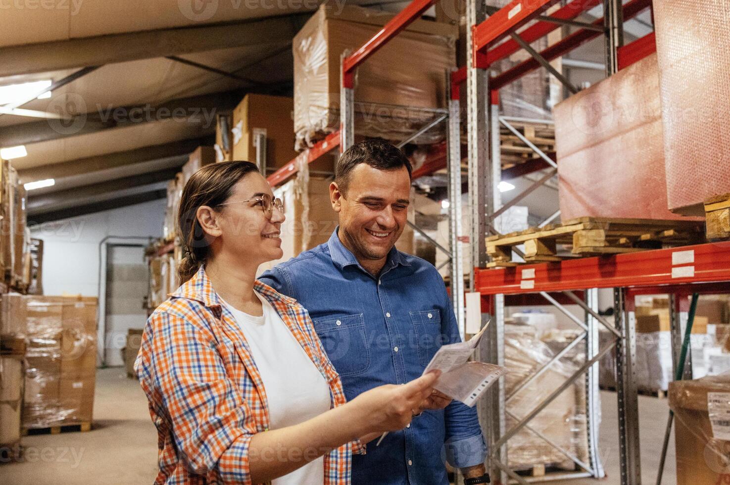 Smiling woman and man in casual clothes mark availability of goods in stock. Man and woman check documentation and goods on shelves. photo