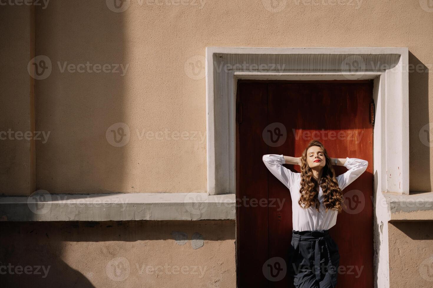 Businesswoman relaxing with hands behind head against door in sunlight photo
