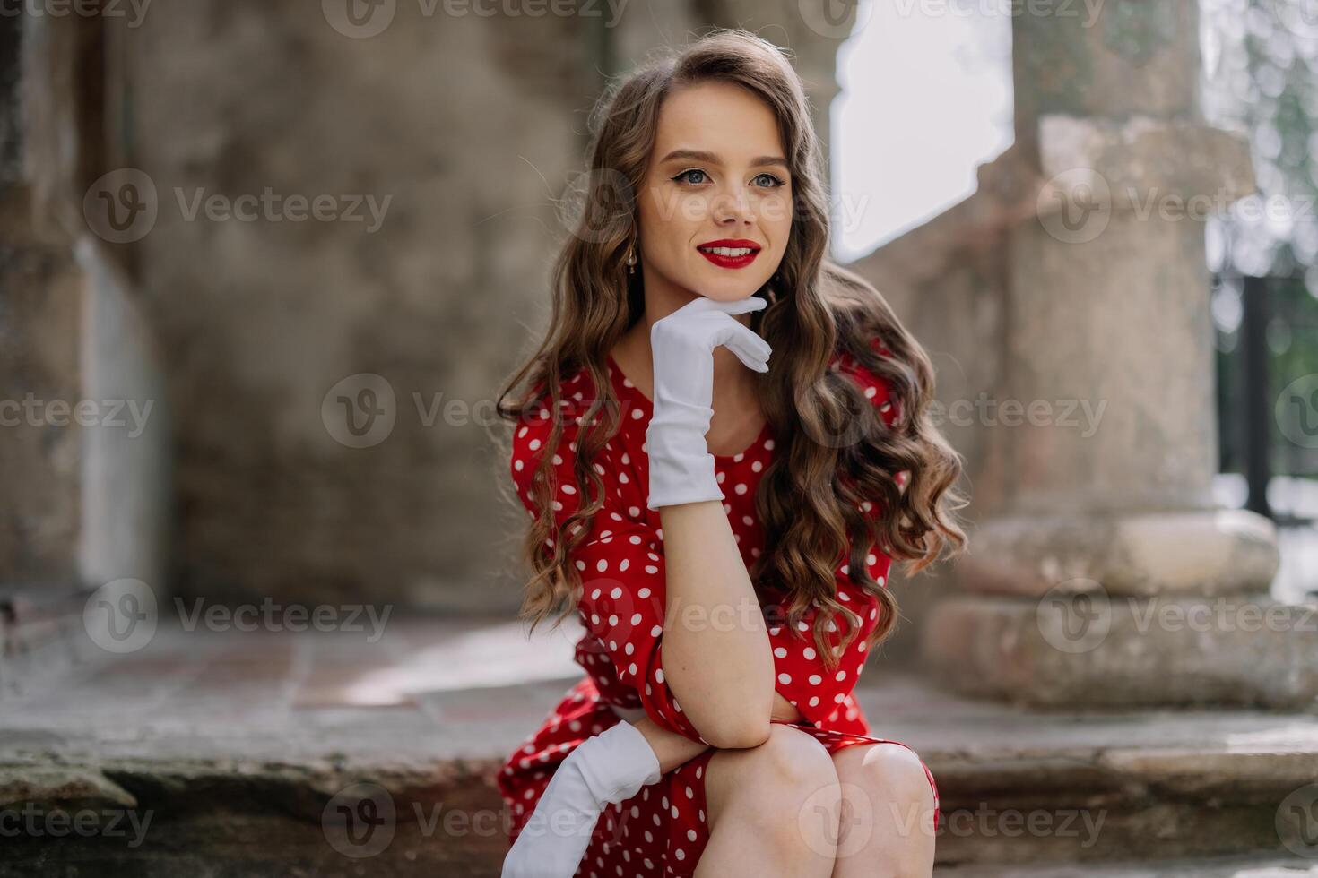 Elegant woman in red polka dot dress and white gloves posing on stone steps photo